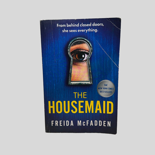 Front cover view of The Housemaid by Freida McFadden centered on a neutral light gray background. Creasing on the top left corner and near the spine.