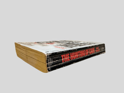 Close-up spine view of The Hunting of Cain by Dan E. Moldea centered on a neutral light gray background. Spine shows creasing and rubbing.