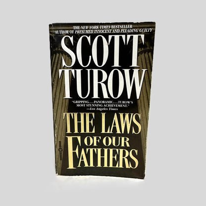 Front cover view of The Laws of Our Fathers by Scott Turow centered on a neutral light gray background. Some minor chipping around the cover edges.