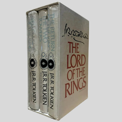 View of all three books in the box sleeve. Three-volume hardcover box set of 'The Lord of the Rings' by J.R.R. Tolkien featuring 'The Fellowship of the Ring,' 'The Two Towers,' and 'The Return of the King'. Dust jackets are present and show creasing. The box is in very good condition.