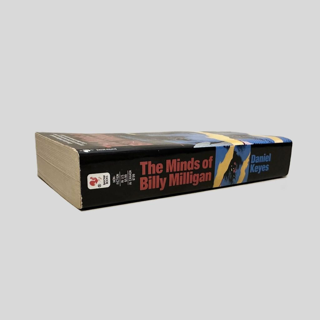 Close-up spine view of The Minds of Billy Milligan by Daniel Keyes centered on a neutral light gray background. The spine is square and shows minimal creasing.