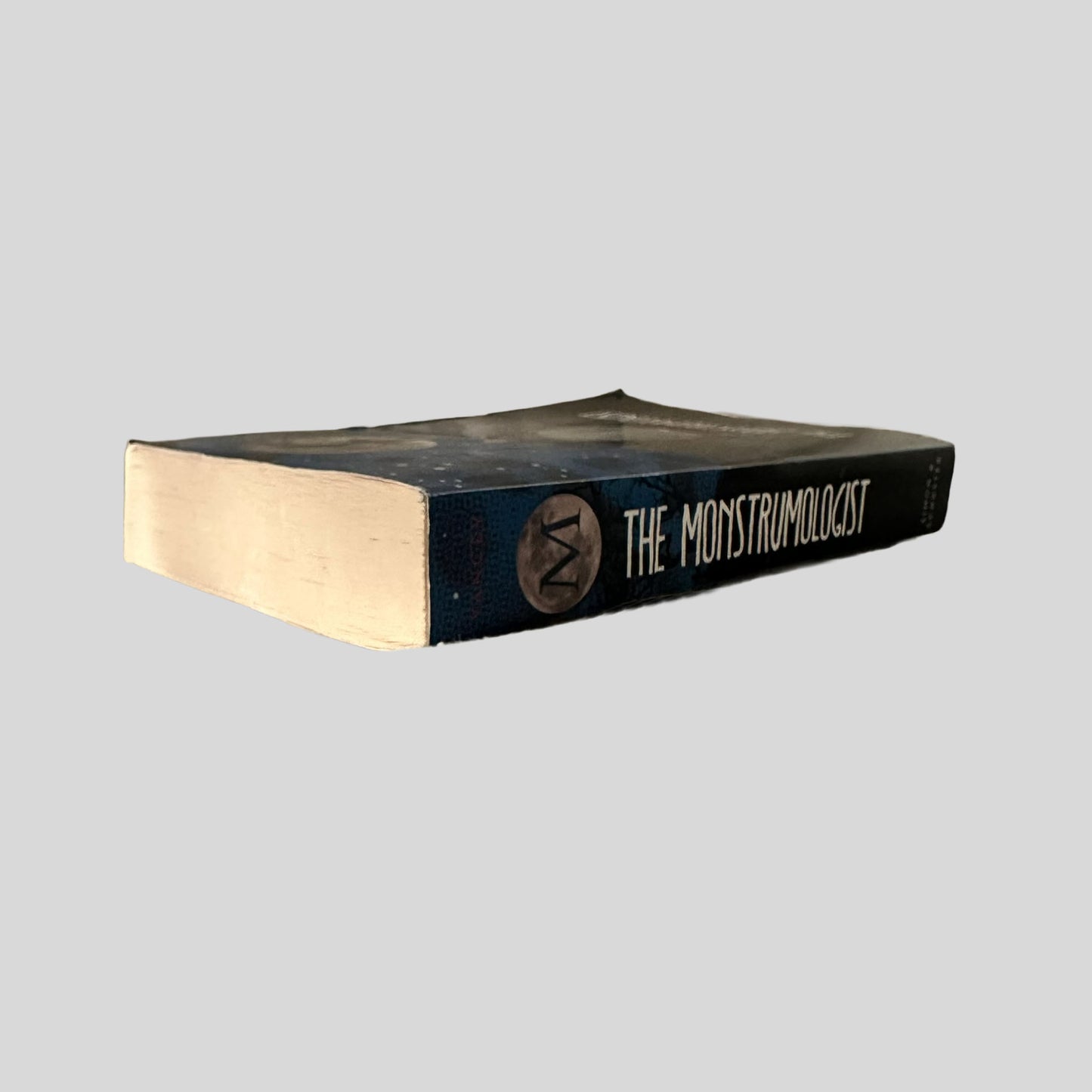 Close-up spine view of The Monstrumologist by Rick Yancey centered on a neutral light gray background. 