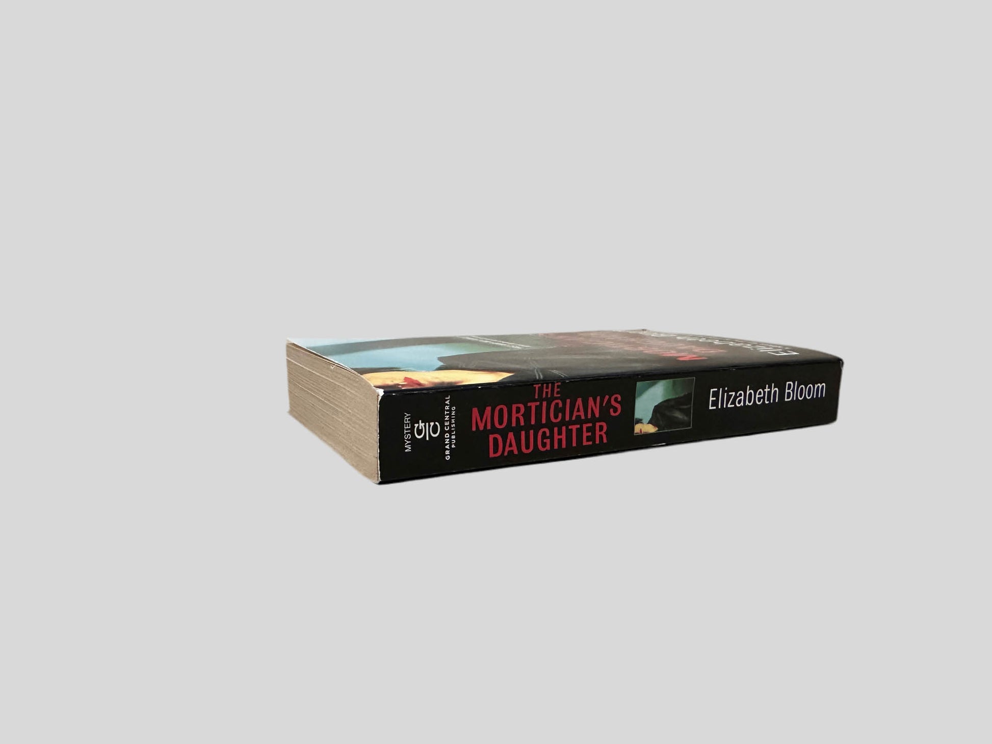 Close-up spine view of The Mortician's Daughter by Elizabeth Bloom centered on a neutral light gray background. Spine shows creasing.