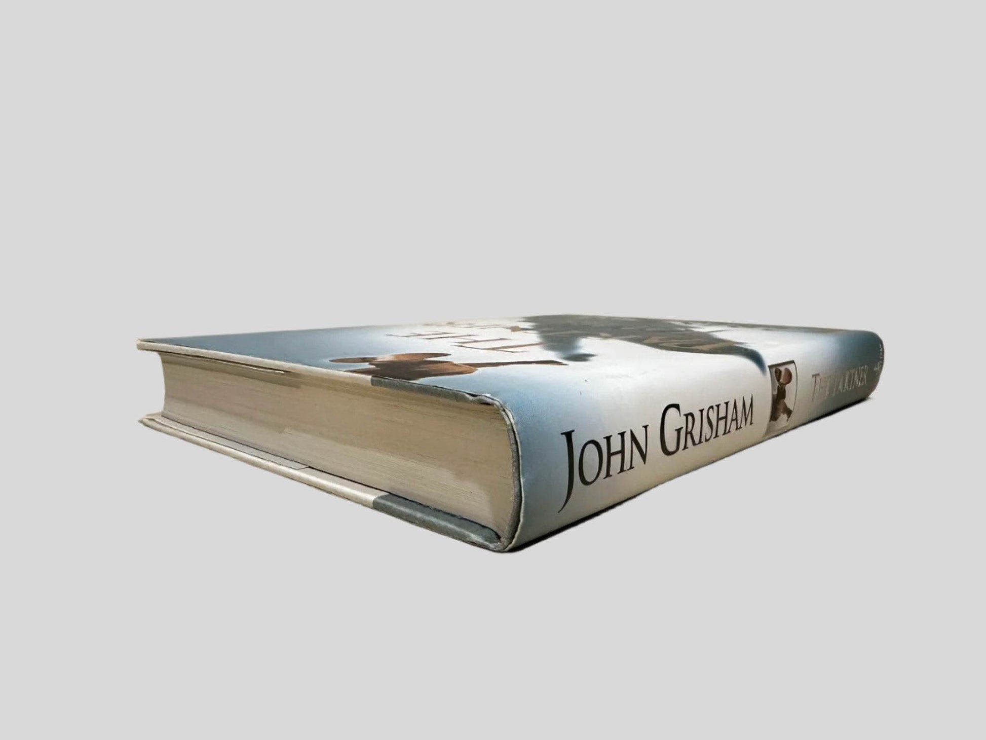 Close-up spine view of The Partner by John Grisham centered on a neutral light gray background. Dust jacket is present and shows no damage. Spine shows no creasing. Pages lay flat.