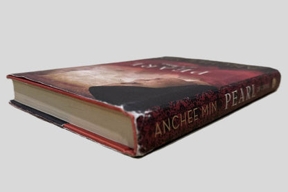 Close-up spine view of The Pearl of China by Anchee Min centered on a neutral light gray background. Spine shows minimal creasing. Pages lay flat. Top of dust jacket is worn at the spine.