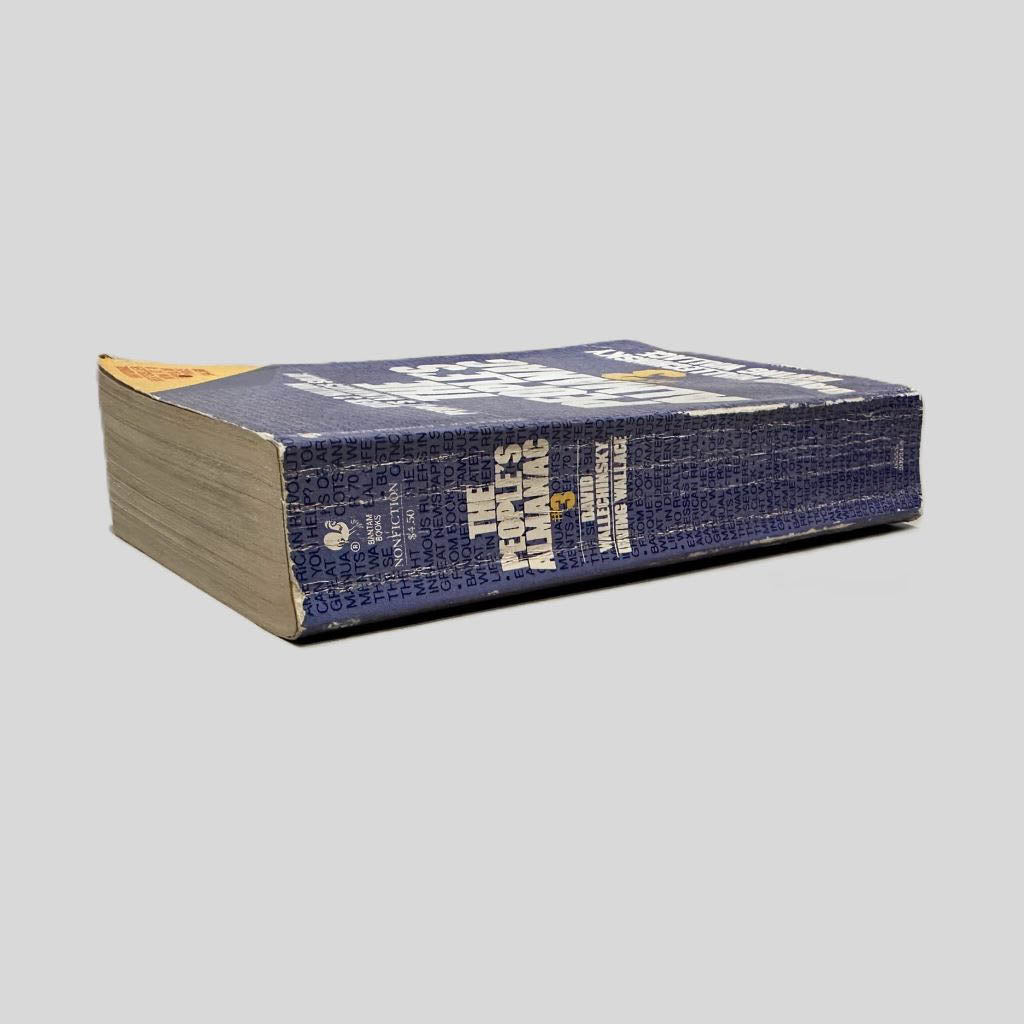Close-up spine view of The People's Almanac #3 edited by David Wallechinsky & Irving Wallace centered on a neutral light gray background. Spine shows creasing; chipping at the top and bottom of spine. Pages lay flat.