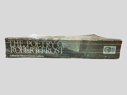 Close-up spine view of The Poetry of Robert Frost: The Collected Poems, Complete and Unabridged centered on a neutral light gray background. Spine shows creasing and chipping. Pages lay flat.