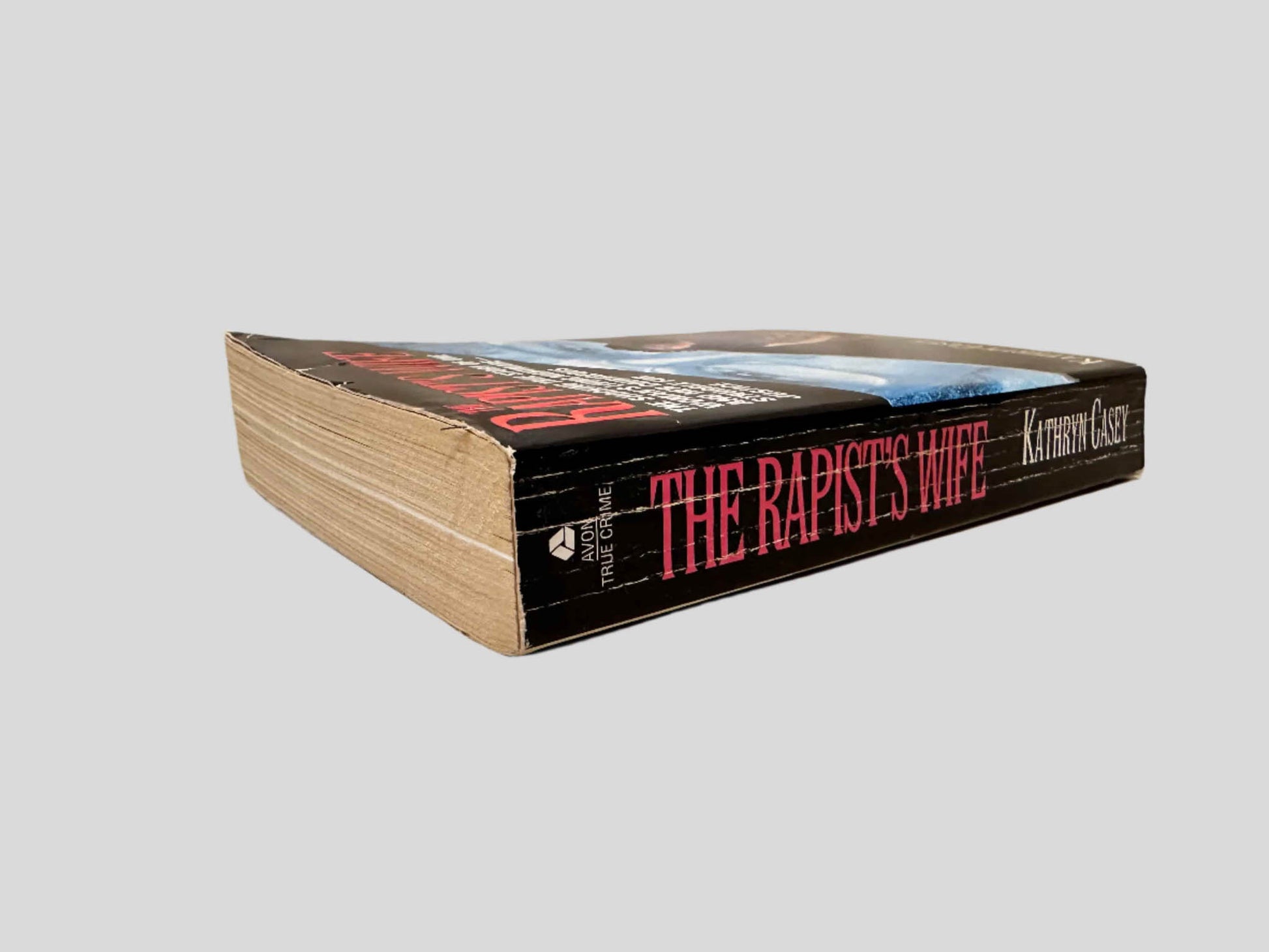 Close-up spine view of The Rapist's Wife by Kathryn Casey centered on a neutral light gray background. Spine shows creasing.