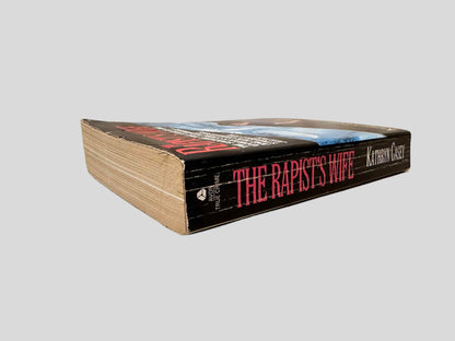 Close-up spine view of The Rapist's Wife by Kathryn Casey centered on a neutral light gray background. Spine shows creasing.