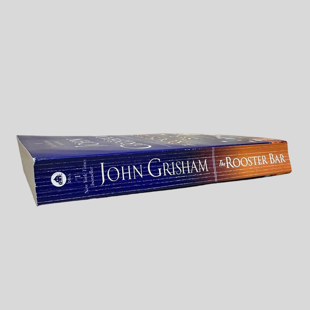Close-up spine view of The Rooster Bar by John Grisham centered on a neutral light gray background. Spine shows creasing.