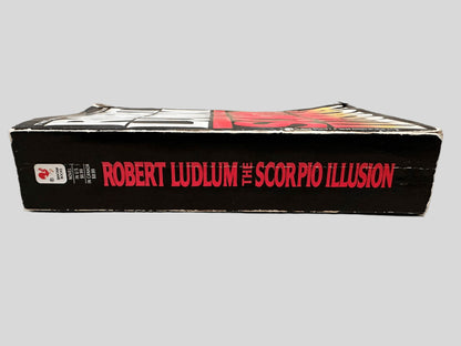 Close-up spine view of The Scorpio Illusion by Robert Ludlum centered on a neutral light gray background. Spine is square and shows minimal creasing. 