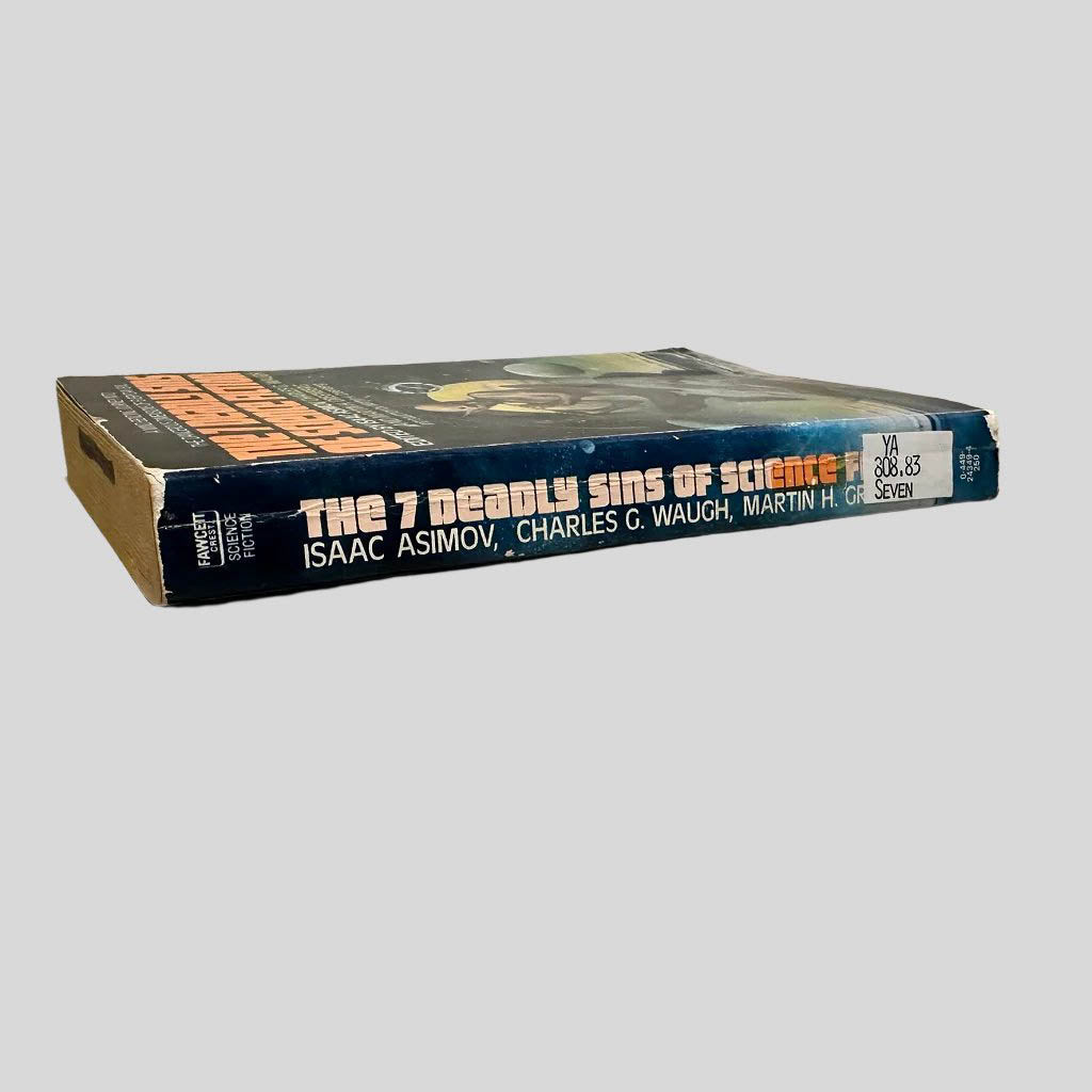 Close-up spine view of The Seven Deadly Sins of Science Fiction Edited By Isaac Asimov centered on a neutral light gray background. Spine is square and shows creasing; chipping at the top and lower end of the spine. Library shelving sticker attached to the lower end of the spine. Pages lay flat.