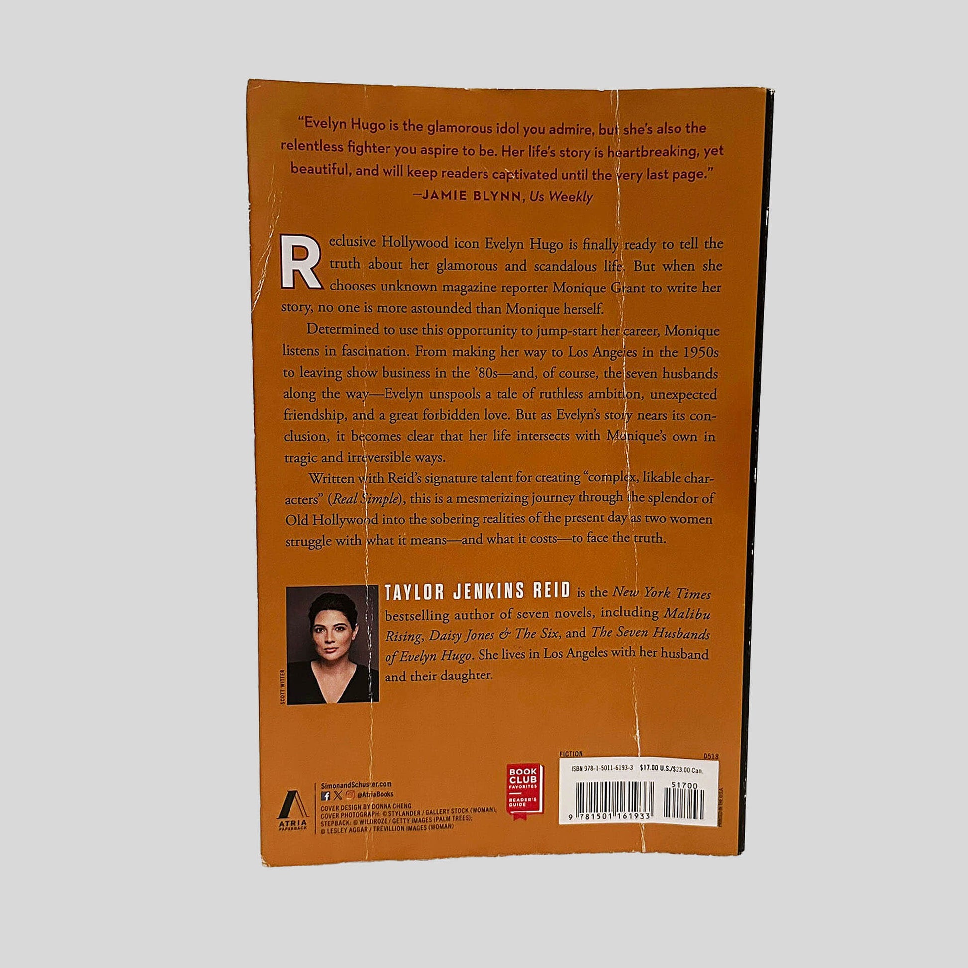 Back cover view of The Seven Husbands of Evelyn Hugo by Taylor Jenkins Reid centered on a neutral light gray background. Two vertical creases are present on the back cover. 