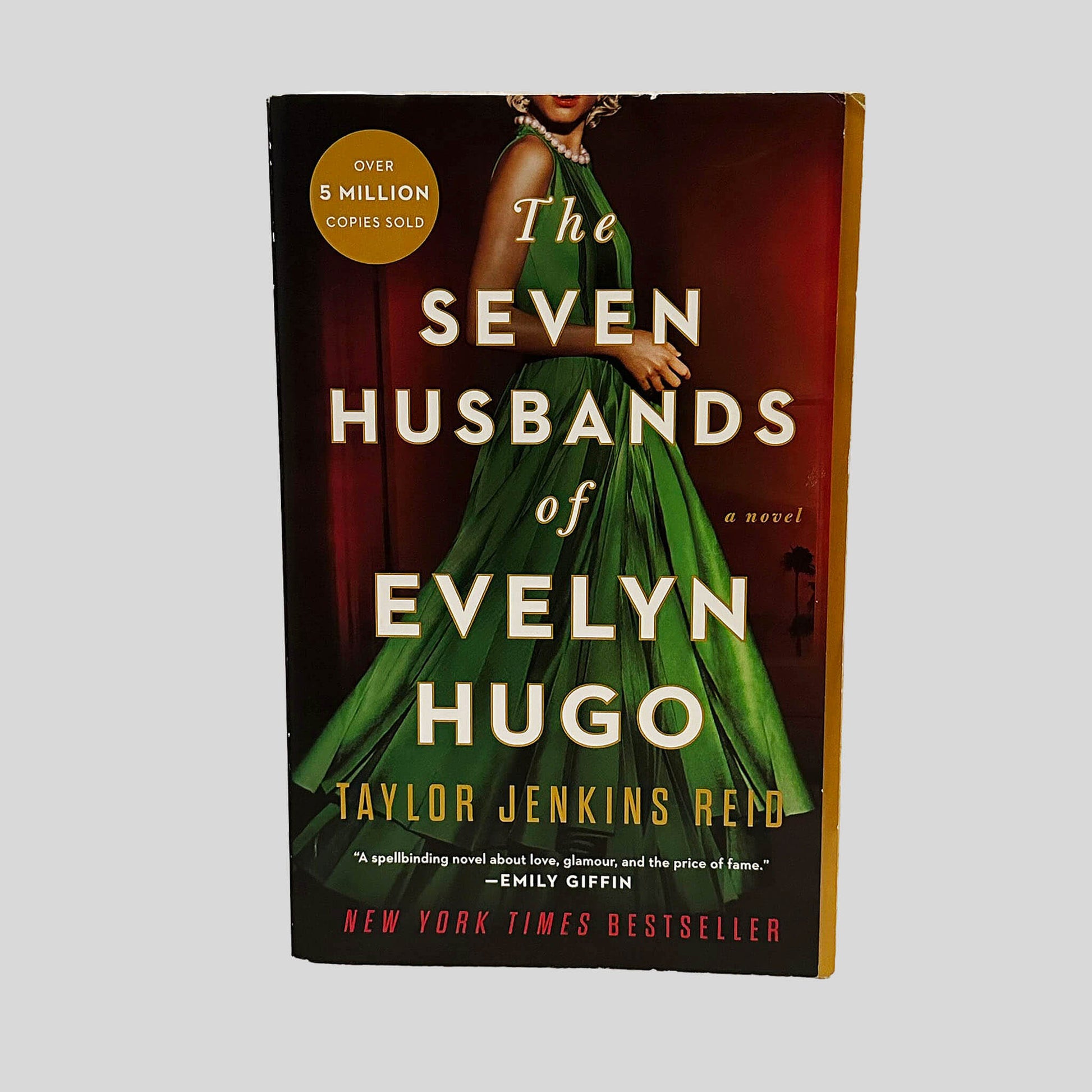 Front cover view of The Seven Husbands of Evelyn Hugo by Taylor Jenkins Reid centered on a neutral light gray background. Minor chipping from normal wear is present around the edges. The cover art is vibrant.
