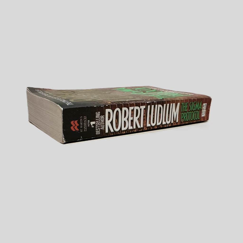 Close-up spine view of The Sigma Protocol by Robert Ludlum centered on a neutral light gray background. Spine is square and shows minimal creasing. Pages lay flat.