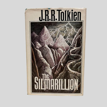 Front cover view of  The Silmarillion by J.R.R. Tolkien (First Edition 1977) centered on a neutral light gray background. Dust jacket is present. Chipping and creasing along the top of the dust jacket.