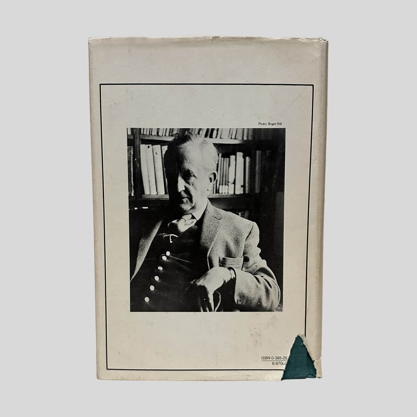 Back cover view of The Silmarillion by J.R.R. Tolkien (First Edition 1977) centered on a neutral light gray background. Chipping is present along the top edges of the dust jacket. A larger triangle shape tear in the bottom left corner of the dust jacket where the ISBN number is printed on the jacket. The green fabric of the book cover can be seen.