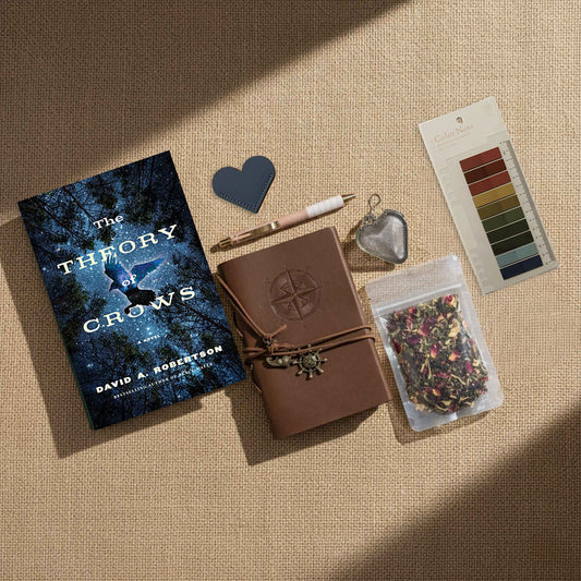 Bathed in dramatic, directional light that mimics the long shadows of a Highland sunset, the "Ultimate Bundle" is the definitive kit for the wayfinding scholar. A weathered, dark-wood leather journal embossed with a compass and draped in ancient nautical charms rests at the center, paired with the mystical crow-themed novel. Complete with botanical tea, a heart-shaped infuser, and earth-toned annotation tools, the composition creates a sense of high-stakes adventure and scholarly devotion.