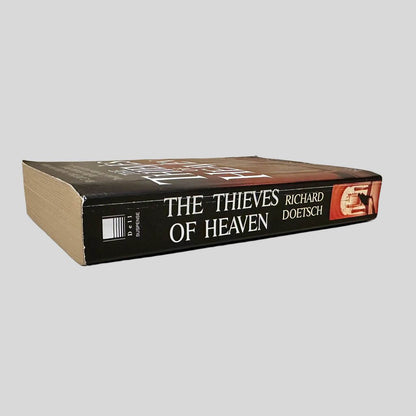 Close-up spine view of The Thieves of Heaven by Richard Doetsch centered on a neutral light gray background. Spine shows creasing.