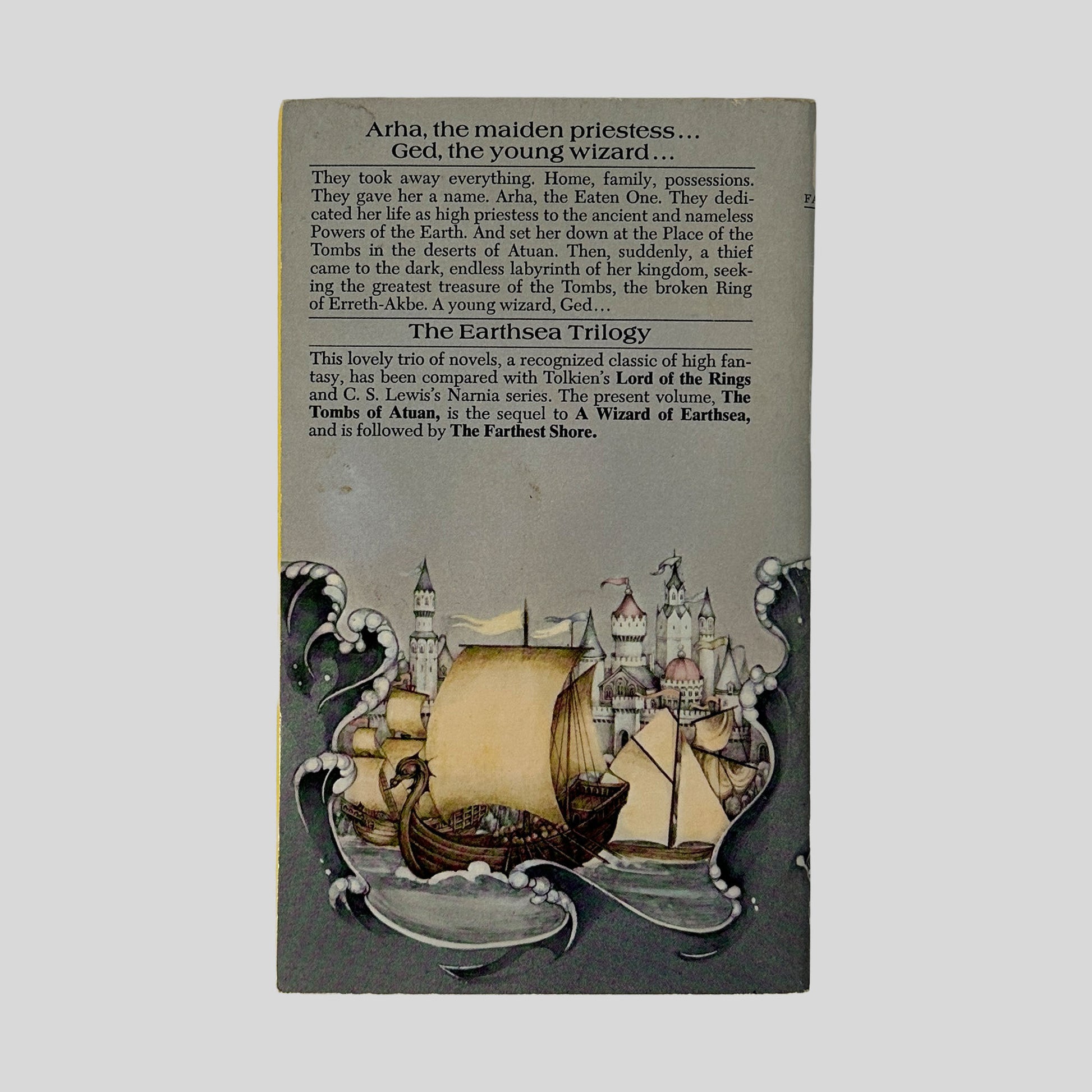 The back cover of the paperback, displaying a plot summary of Arha and Ged's encounter in the Tombs, positioned above a continuation of the front cover's castle and ship artwork.