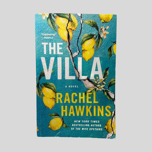 Front cover view of The Villa by Rachel Hawkins centered on a neutral light gray background. Chipping and creasing present along the bottom edge of the cover and near the spine.