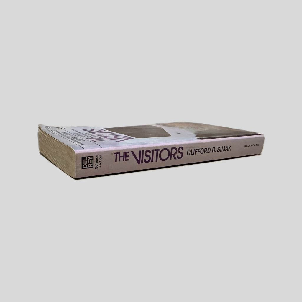 Close-up spine view of The Visitors by Clifford D. Simak centered on a neutral light gray background. Spine shows creasing. Pages lay flat.
