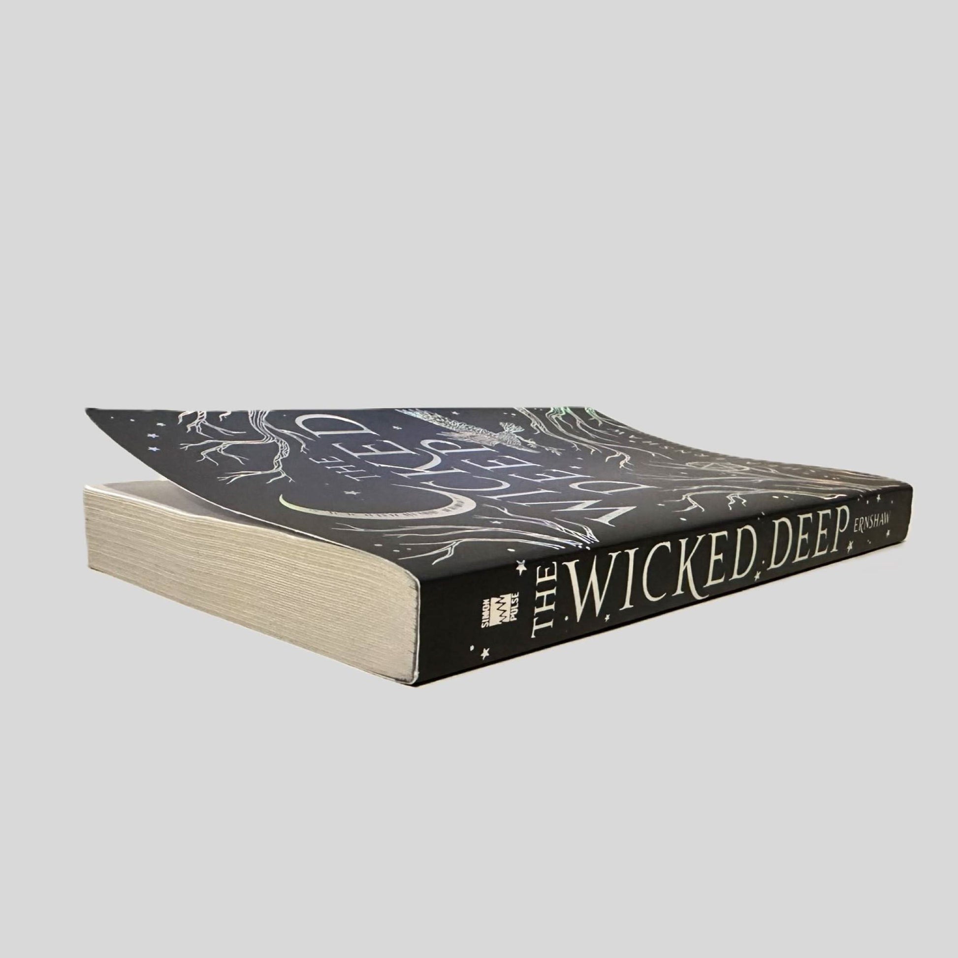 Close-up spine view of The Wicked Deep by Shea Ernshaw centered on a neutral light gray background. Spine is square and shows no creasing. Pages lay flat.