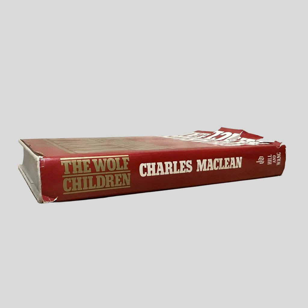 Close-up spine view of The Wolf Children by Charles Maclean centered on a neutral light gray background. Dust jacket is present. Spine shows tears at the top and bottom of the jacket.Pages lay flat.