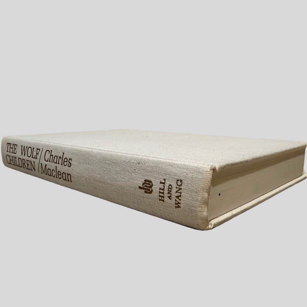 Close-up spine view of The Wolf Children by Charles Maclean with the dust jacket removed, centered on a neutral light gray background. Spine is square and shows zero damage. Pages are tight and lay flat.