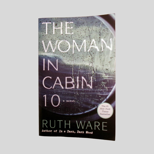 Front cover view of The Woman In Cabin 10 by Ruth Ware centered on a neutral light gray background. Minor chipping to the bottom of the front cover. Cover does not lay flat along the edge. Pages are straight and crisp.