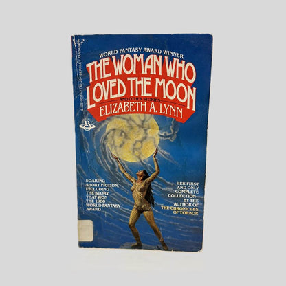 Front cover view of The Woman Who Loved The Moon by Elizabeth A. Lynn centered on a neutral light gray background. Creasing and chipping present around the edges and near the spine.