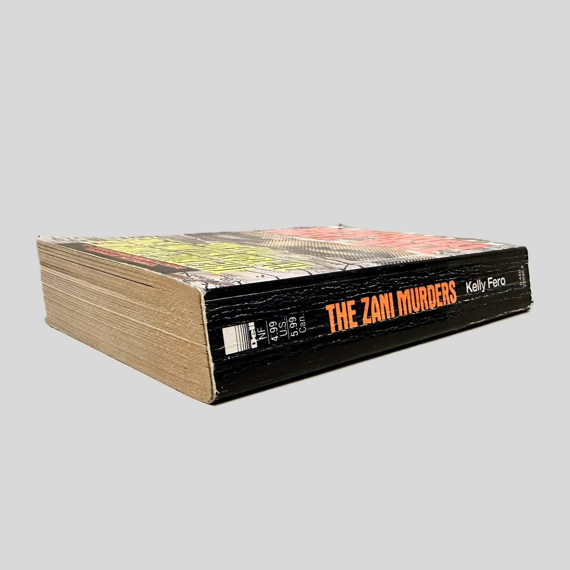 Close-up spine view of The Zani Murders by Kelly Fero centered on a neutral light gray background. Spine is square, shows creasing.