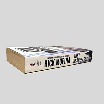 Close-up spine view of They Disappeared by Rick Mofina centered on a neutral light gray background. Spine is square and shows no creasing. Pages lay flat.