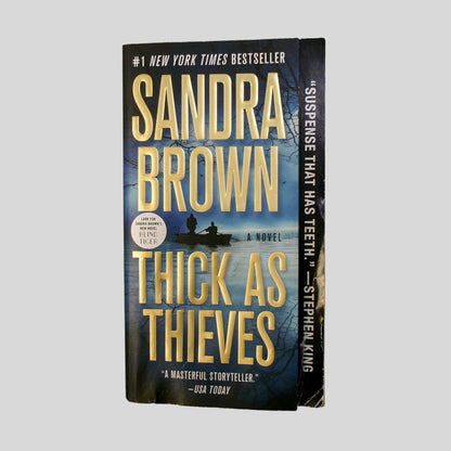 Front cover view of Thick As Thieves by Sandra Brown centered on a neutral light gray background. Chipping and creasing to the bottom left corner. Small dent on the bottom left.