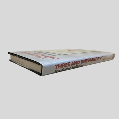 Close-up spine view of Three and One Make Five by Roderic Jeffries centered on a neutral light gray background. Dust jacket is present and shows no damage. Spine shows no creasing. Pages lay flat.