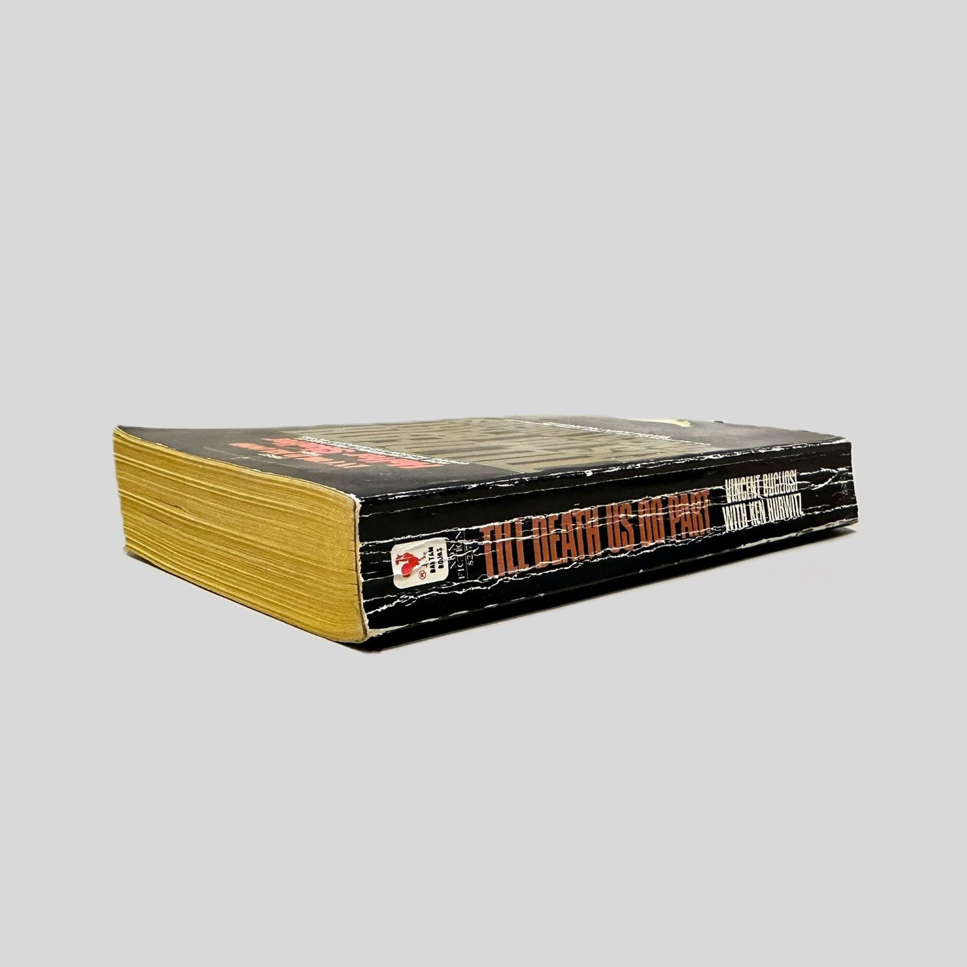 Close-up spine view of Till Death Us Do Part by Vincent Bugliosi & Ken Hurwitz centered on a neutral light gray background. Spine is square and shows creasing.