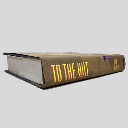 Close-up spine view of To the Hilt by Dick Francis centered on a neutral light gray background. Spine shows creasing. Dust jacket is present with no visible damage.
