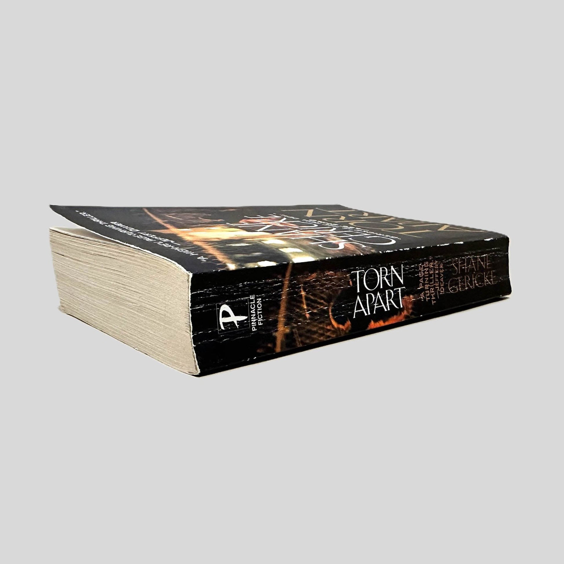 Close-up spine view of Torn Apart by Shane Gericke centered on a neutral light gray background. Spine shows creasing. Pages lay flat.