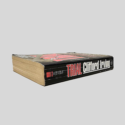 Close-up spine view of Trial by Clifford Irving centered on a neutral light gray background. Spine shows creasing and some chipping at the top of the spine. Pages lay flat.
