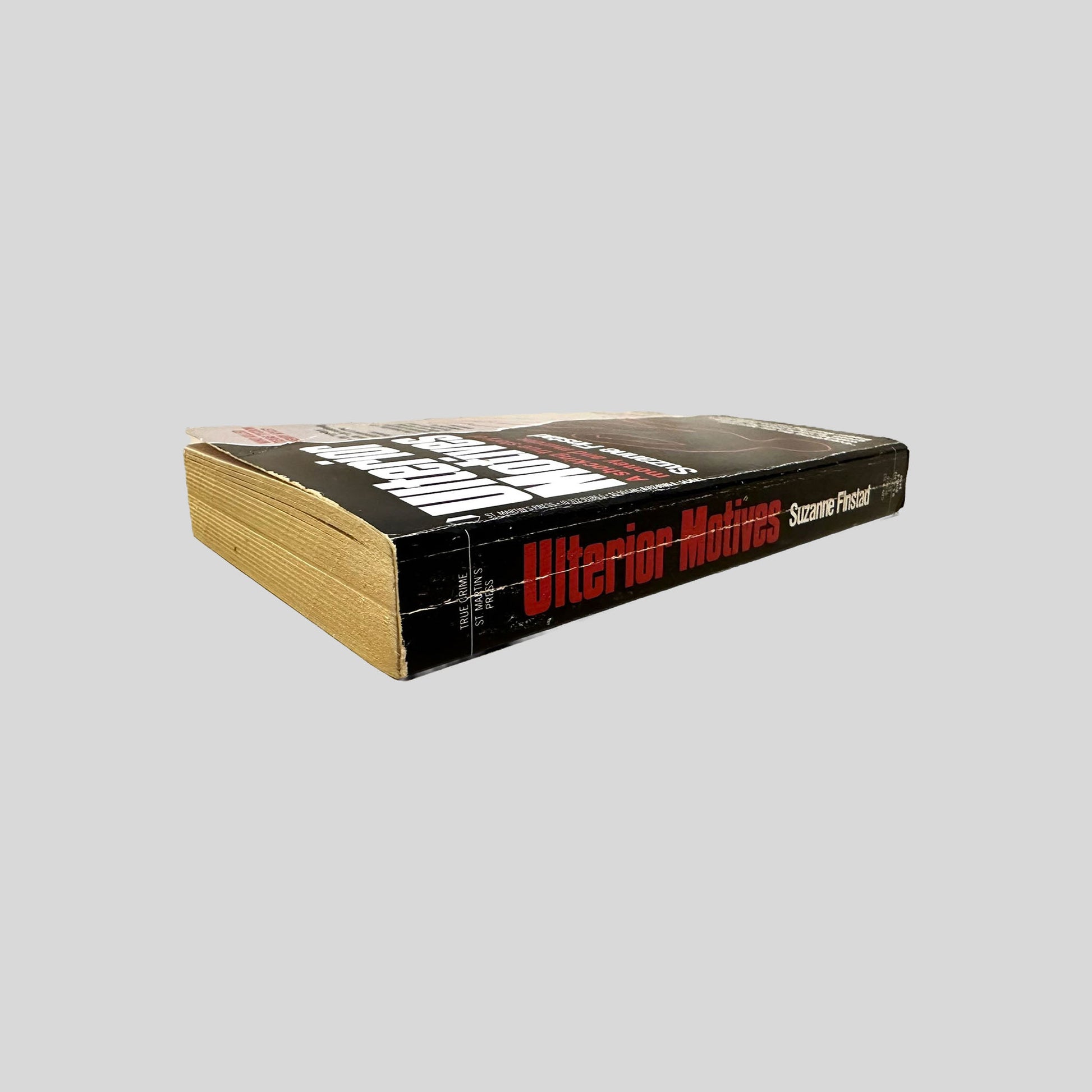 Close-up spine view of Ulterior Motives by Suzanne Finstad centered on a neutral light gray background. 