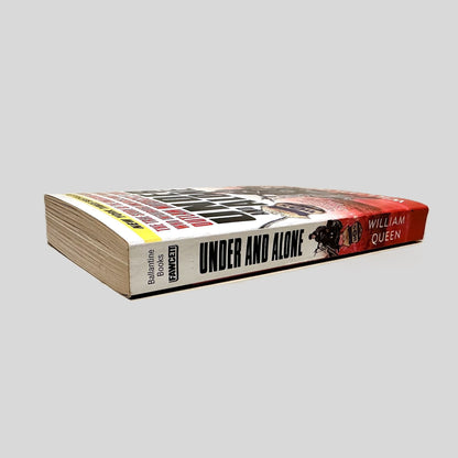 Close-up spine view of Under and Alone by William Queen centered on a neutral light gray background. Spine is square and shows minimal creasing.