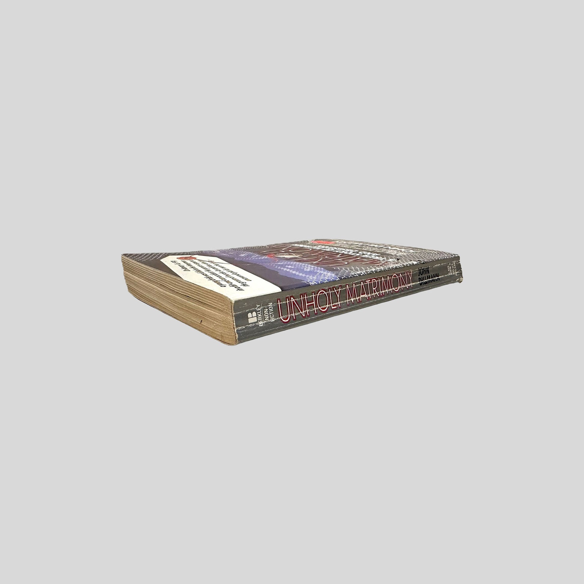 Close-up spine view of Unholy Matrimony by John Dillmann centered on a neutral light gray background. 