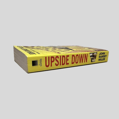 Close-up spine view of Upside Down by John Ramsey Miller centered on a neutral light gray background. Spine is square and shows minimal creasing.