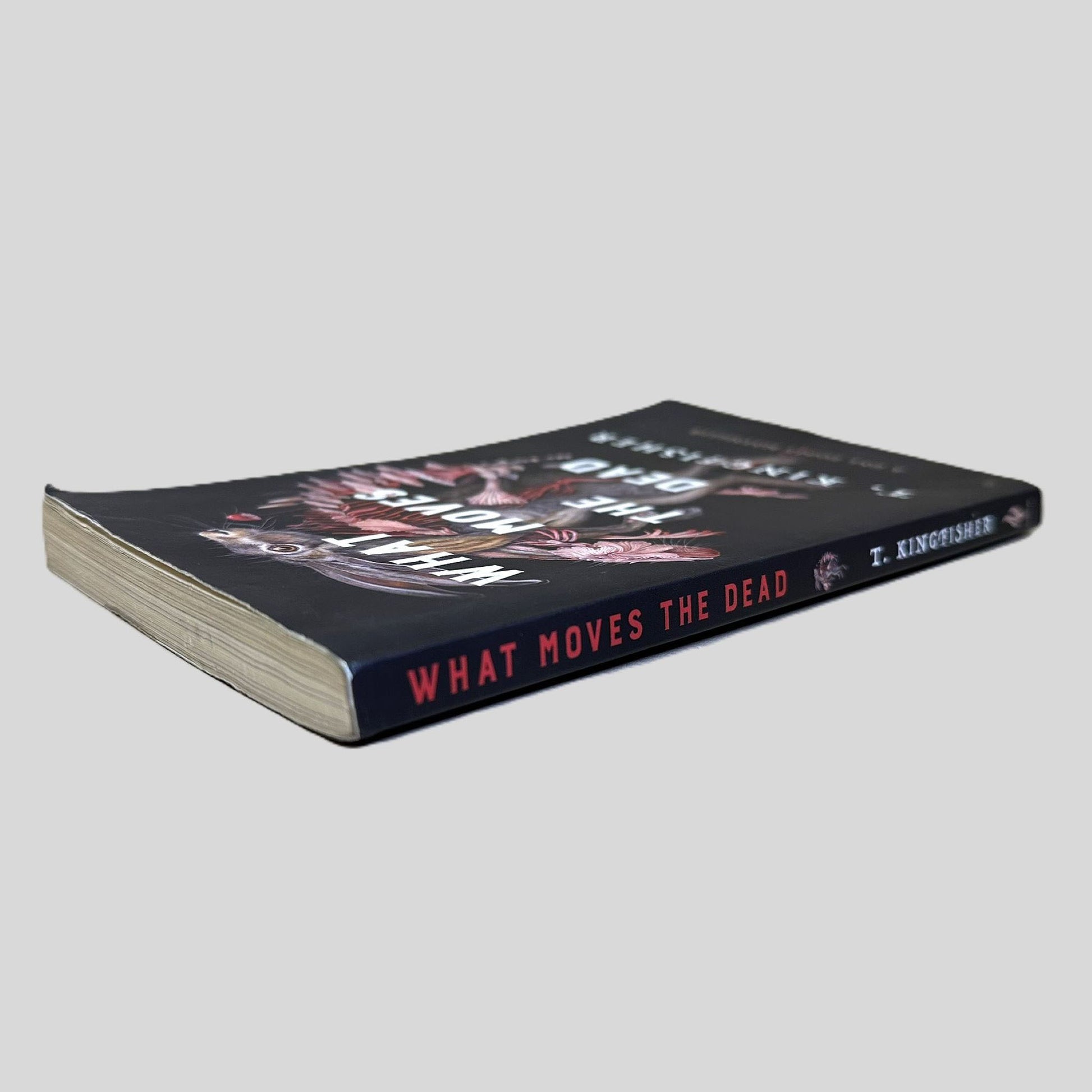 Close-up spine view of What Moves The Dead by T. Kingfisher centered on a neutral light gray background. 