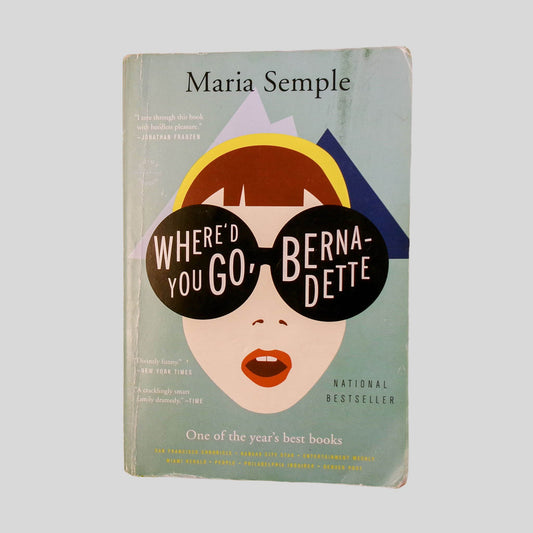 Front cover view of Where'D You Go, Bernadette by Maria Semple centered on a neutral light gray background. Chipping and creasing are present to the front cover. Staining in the top right corner. Cover art is clear and vibrant.