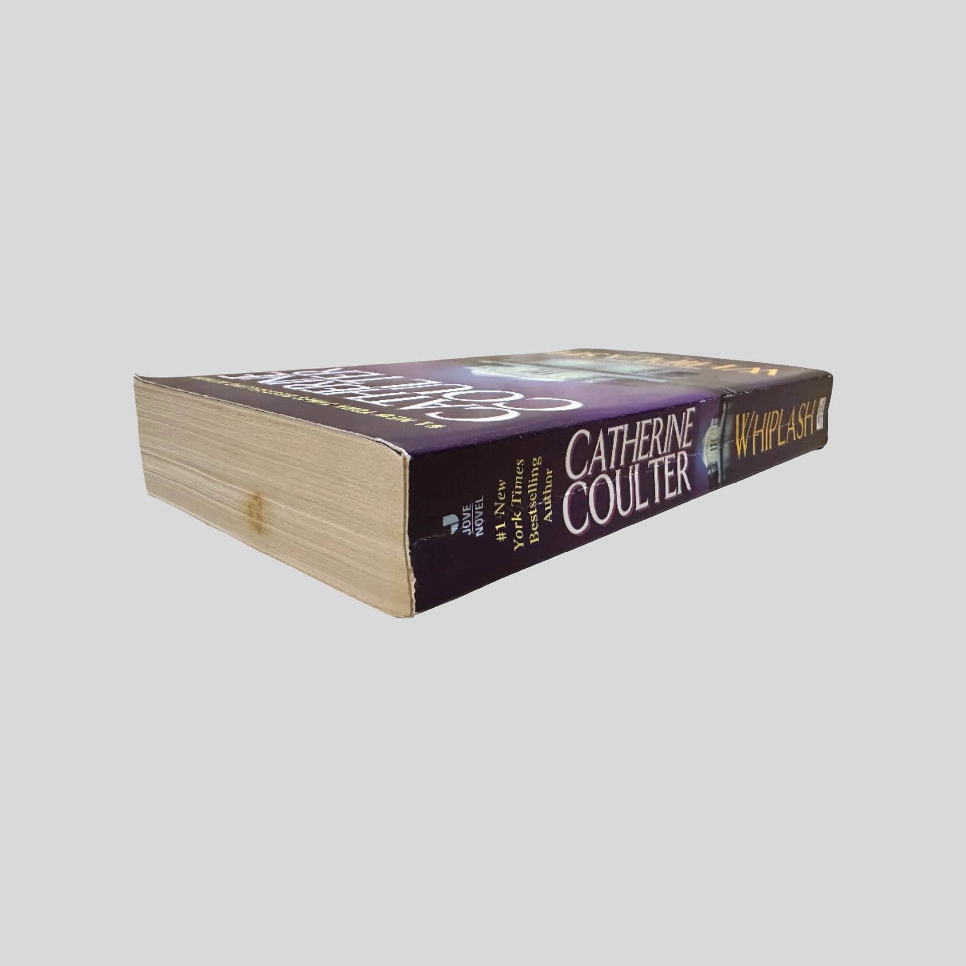 Close-up spine view of Whiplash by Catherine Coulter centered on a neutral light gray background. Spine shows creasing. Pages lay flat. 