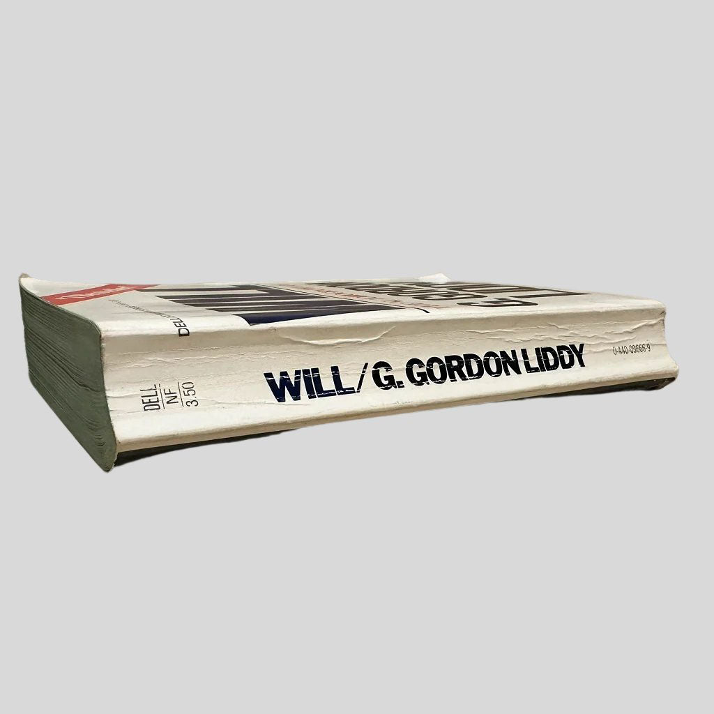 Close-up spine view of Will by G. Gordon Liddy centered on a neutral light gray background. Spine shows creasing and cocking.