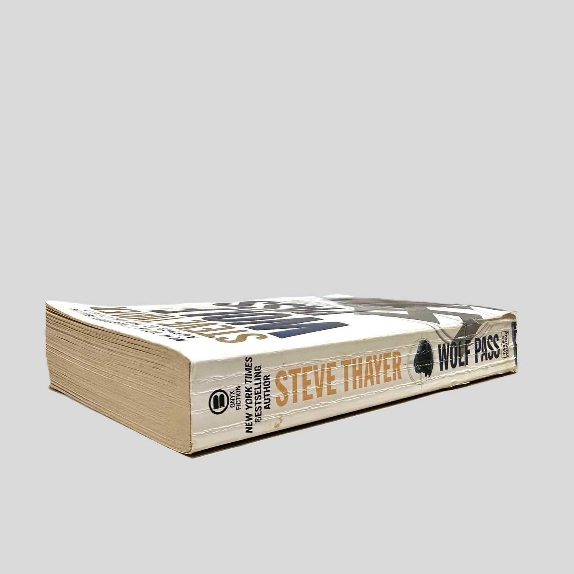 Close-up spine view of Wolf Pass by Steve Thayer centered on a neutral light gray background. Spine shows creasing and chipping on the lower front corner.