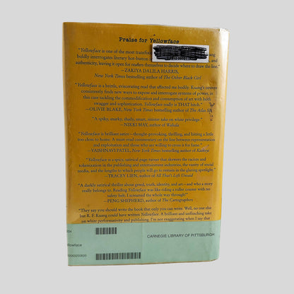 Back cover view of Yellowface by R. F. Kuang centered on a neutral light gray background. Dust jacket is present, in a mylar cover. Library barcode sticker in the top right, covered with black marker.
