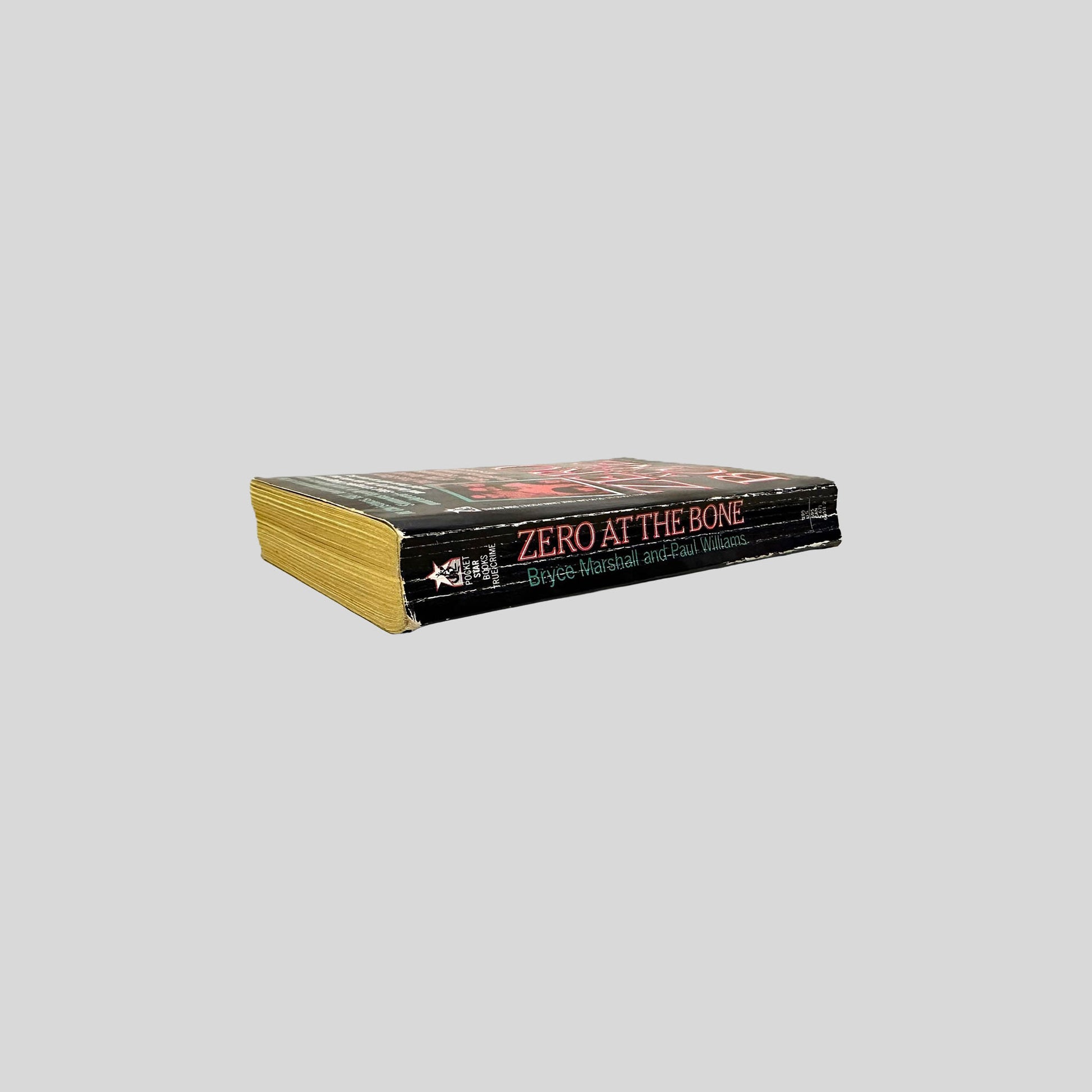 Close-up spine view of Zero at the Bone by Bryce Marshall and Paul Williams centered on a neutral light gray background. 